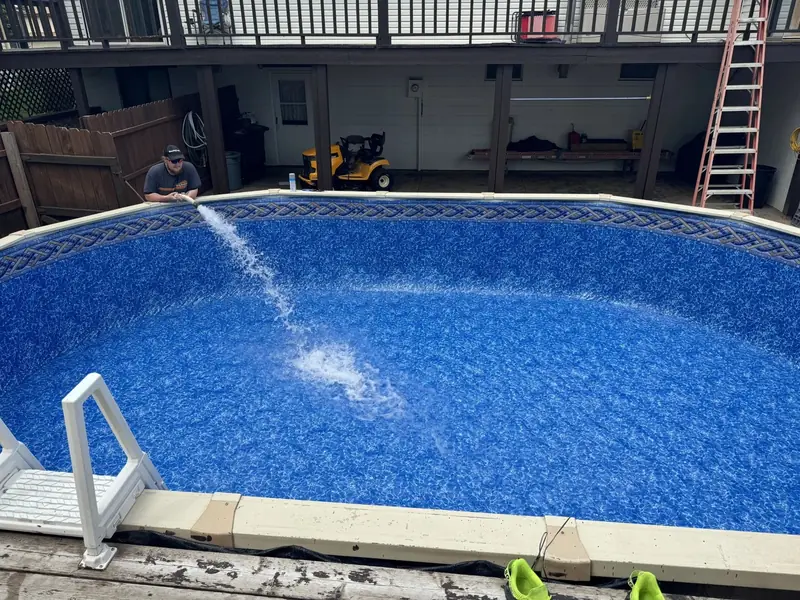 Above-ground pool filling up, with the return jet spraying water and a garage behind