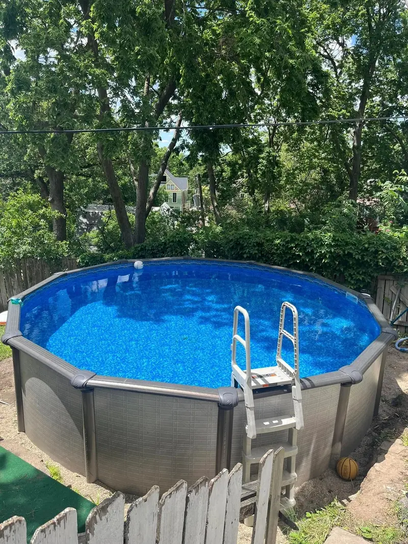 Finished round above-ground pool with a ladder, surrounded by trees