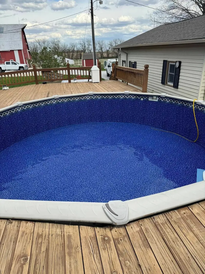 View from a deck over an above-ground pool with a deep blue patterned liner and a rolled-up cover