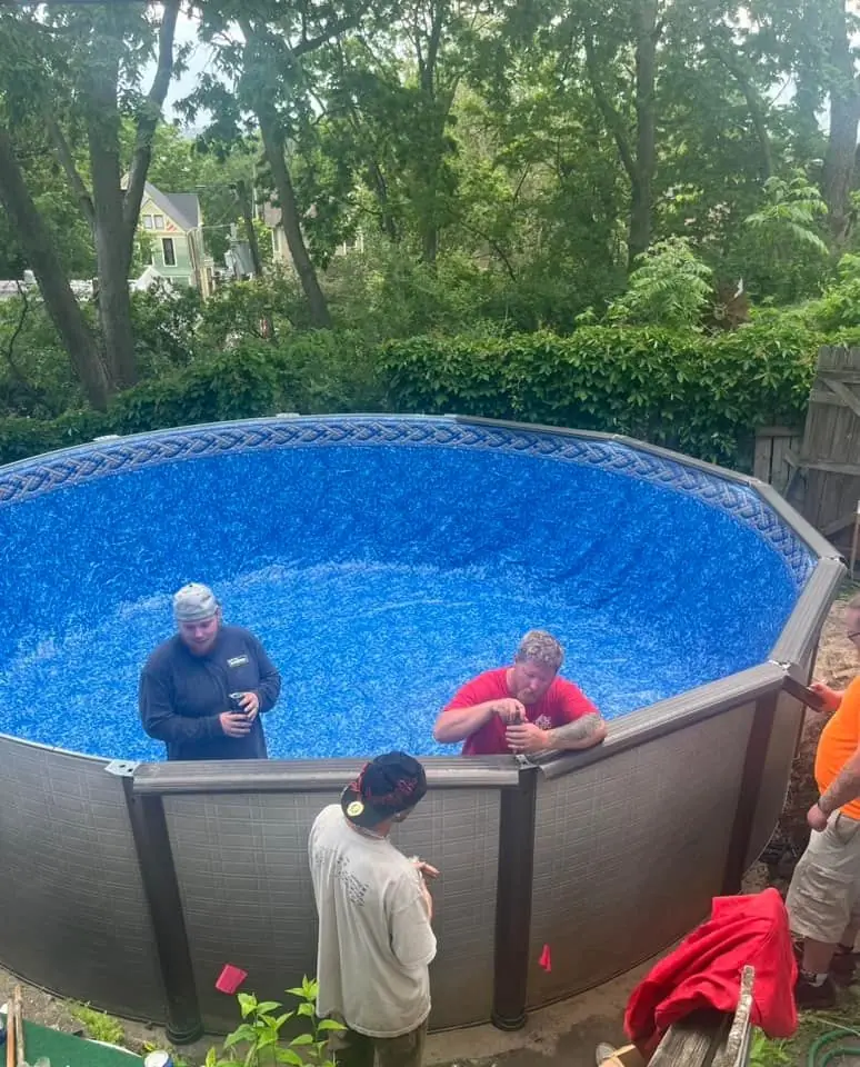Pool Rx crew of four setting a blue patterned liner inside a new above-ground pool wall in a wooded backyard