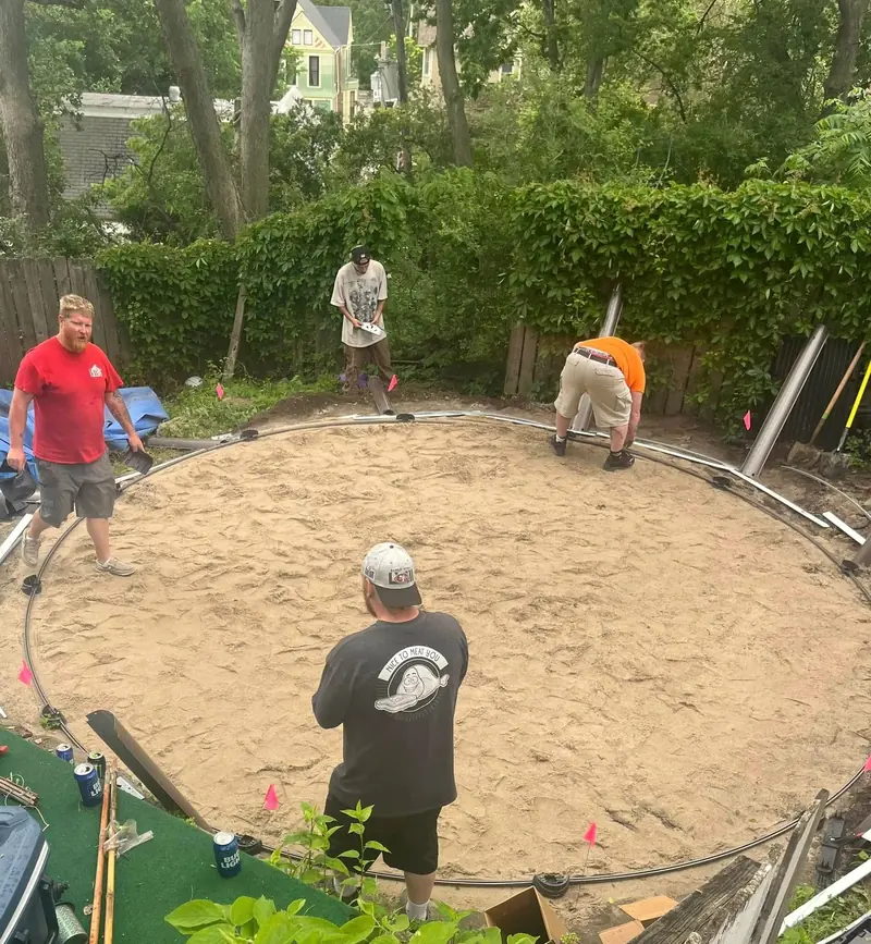 Pool Rx crew leveling a round sand base and laying the bottom track for an above-ground pool, pink marker flags around the edge