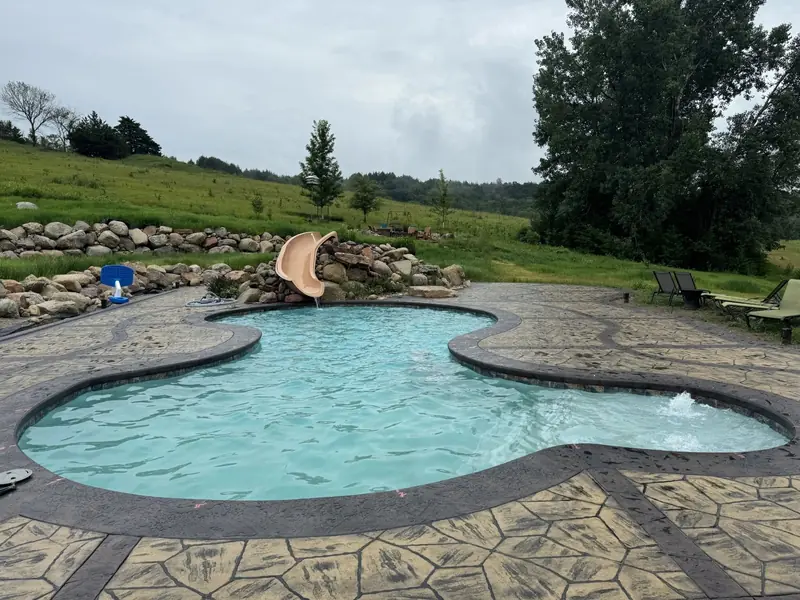 Freeform in-ground pool with a slide, a boulder retaining wall and a stamped concrete deck in the green hills