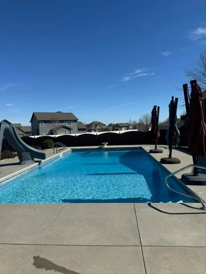 Rectangular in-ground pool with a slide in a newer subdivision under a blue sky