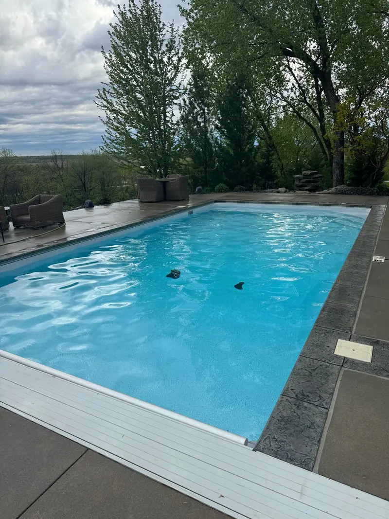 Rectangular in-ground pool with clear blue water, a stamped concrete deck and patio chairs, trees and a wide river-valley view behind it
