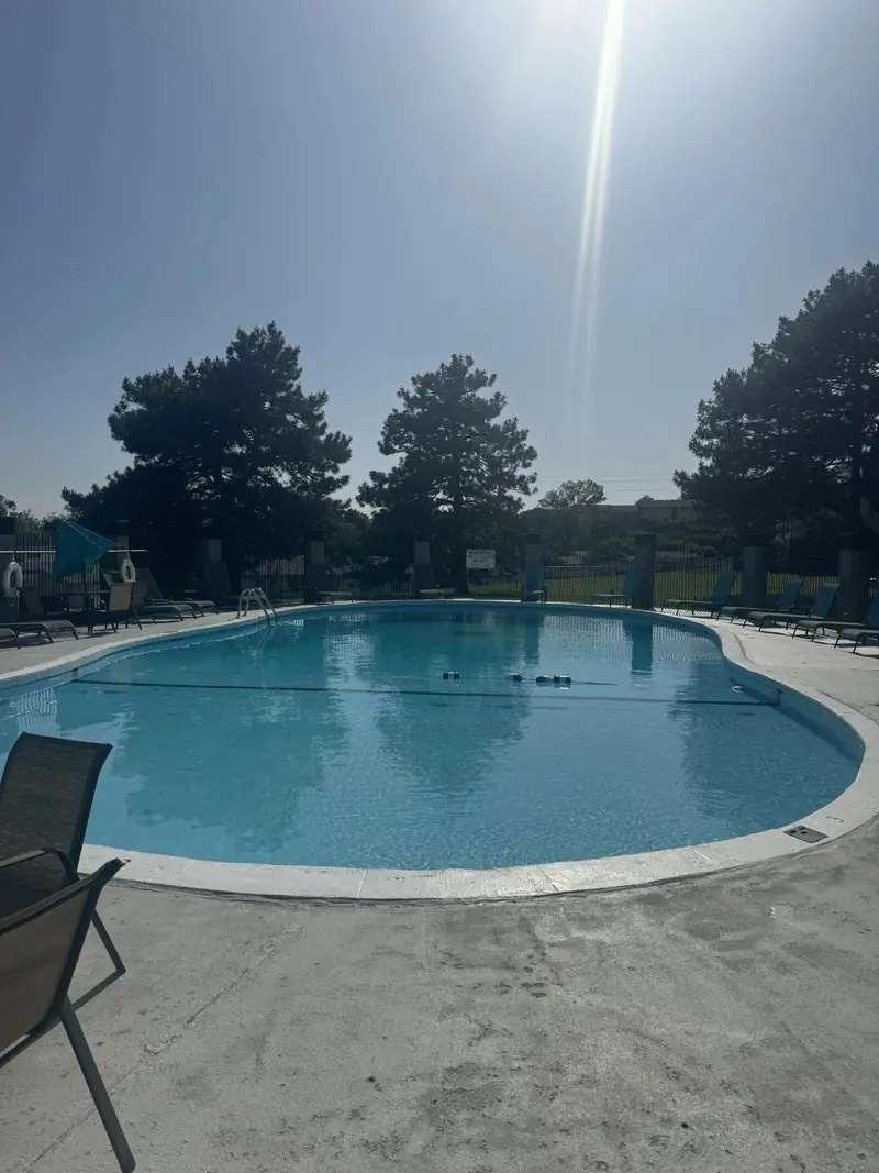 Large kidney-shaped pool with a wide concrete deck and lounge chairs on a bright summer day